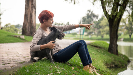 Naklejka na ściany i meble latin woman looking at the horizon with her dog in a park in bogota colombia