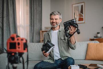 Smiling senior european male with beard shooting blog review on vr glasses in living room interior