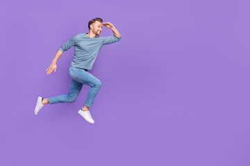 Photo of attractive pretty guy wear grey shirt running fast jumping high looking far away empty space isolated violet color background