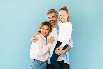 Man Holding Daughter In Arms Embracing Wife On Blue Background