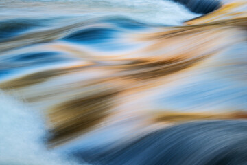 Abstract landscape of a rapids at Bond Falls captured with motion blur and illuminated by reflected color from sunlit autumn maples and blue sky overhead, Michigan's Upper Peninsula, USA 