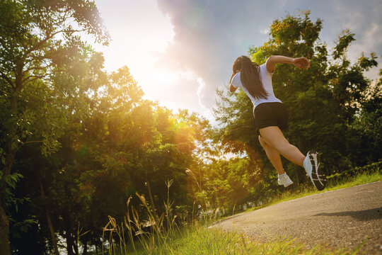 Silhouette of young woman running sprinting on road. Fit runner fitness runner during outdoor workout with sunset background.	