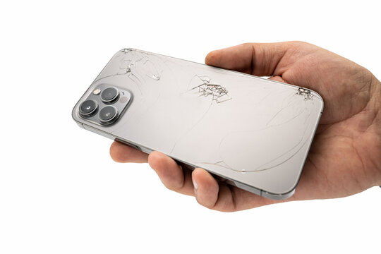 Man hand holding modern smartphone with broken back glass on white background.