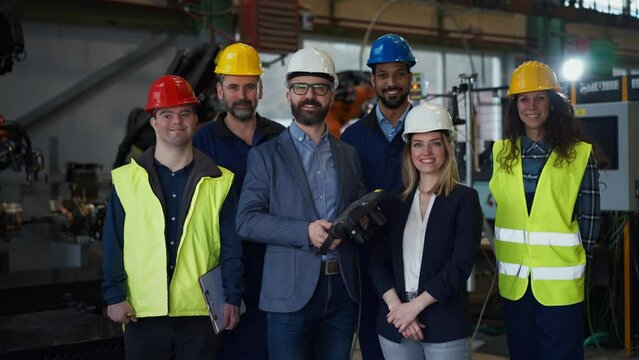 Young man worker with Down syndrome with manager and other collegues working in industrial factory, social integration concept.