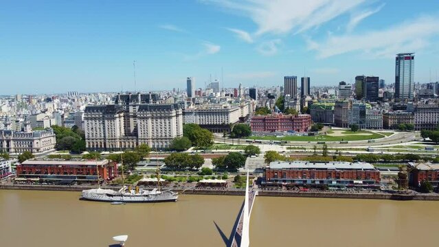 Aerial drone footage of Buenos Aires downtown district with the Casa Rosada, the Plaza de Mayo and the Woman's bridge over the Puerto Madero harbor in Argentina capital city with a tilt down motion.  