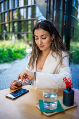 Young business woman sitting outdoors in the city cafe and looking to the watch