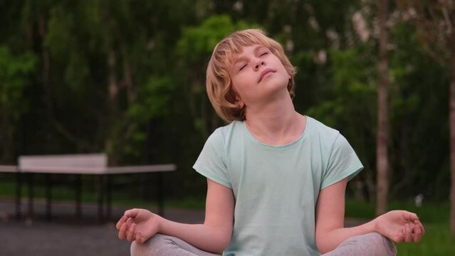 A beautiful teenage girl sits in a lotus position. The girl stretches her neck. The child is doing yoga in nature