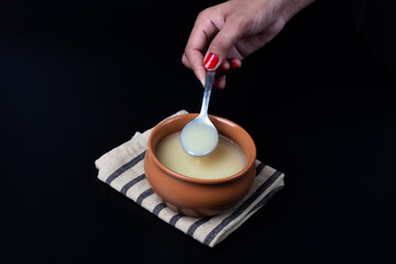 Pure cow ghee in ceramic bowl on black background with ghee spoon in hand