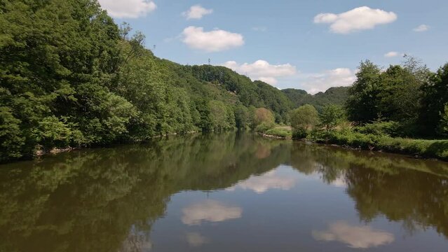 Low drone flight over a wide brown river that reflects the beautiful sky above.