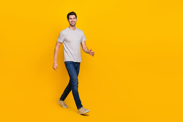 Full length photo of nice brunet millennial guy go wear t-shirt jeans footwear isolated on yellow background