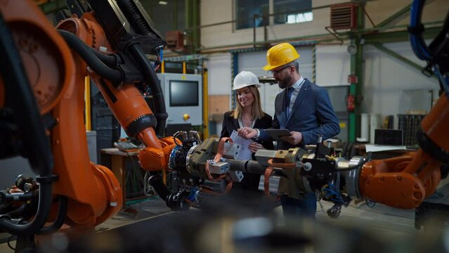 Chief engineer and project manager in modern industrial factory with robot arms talking and planning optimization of production.