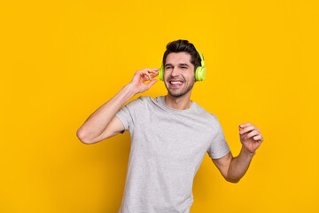 Photo of funny brunet young guy enjoy music look up wear earphones grey t-shirt isolated on yellow color background