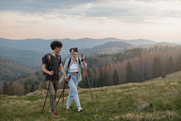 Portrait of young happy couple of tourists walking the mountains chain with sticks. Landscape.