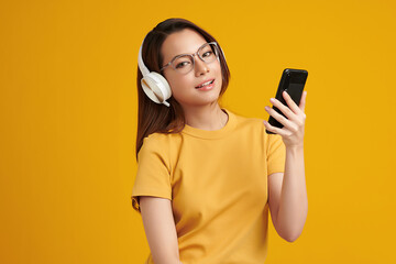 Happiness Beautiful Asian smiling young woman wearing technology wireless  headphones for listening the music via smart mobile phone on yellow background,