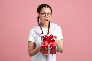 Happy pretty young woman holding gift box on pink background, blank copy space for your advertising content.