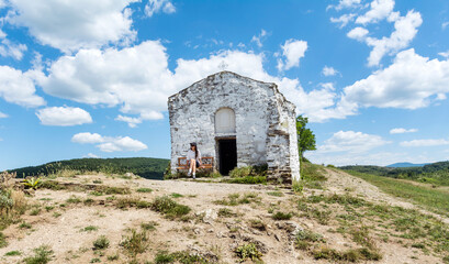 Traveler woman sitting on a bench in front of white stone chapel in Bulgaria 