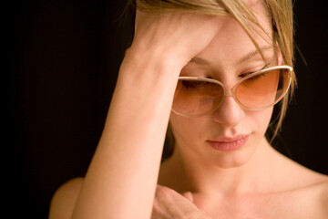 A confident young female model wearing retro sunglasses. Head and shoulder casual studio portrait of a beautiful woman set against black.