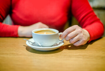 A girl drinks coffee at a table in a cafe

