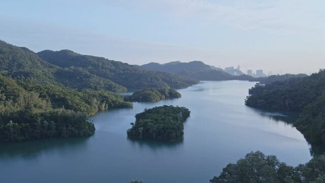 A dynamic ascending aerial shot of the mountains next to the dam and control tower of Shing Mun Reservoir in Hong Kong. It is located in Shing Mun, the area between Tsuen Wan and Sha Tin.