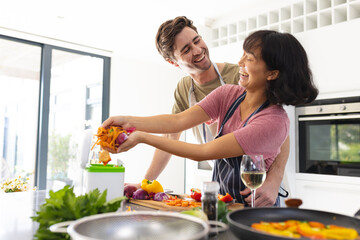 Happy caucasian boyfriend looking at asian girlfriend throwing vegetable peels in compost bin