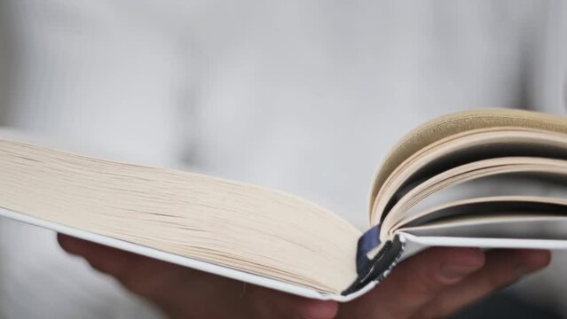 Young man reading a book and turning pages, close up, slow motion. Male hands holding a book and flips through the pages. An unrecognizable man in blur studying the text. Learning, Self-education. 4K