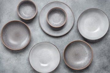 Empty gray craft plates and bowls. Handmade ceramics. Gray grunge background. Top view, flat lay.