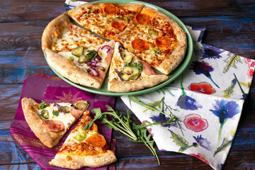 Slices of Chorizo Pizza and Bacon Pizza with pickled cucumbers on wooden table.