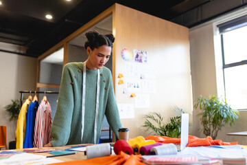 Biracial female fashion designer working at desk in studio