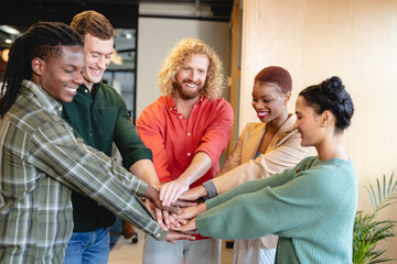 Happy diverse fashion designers stacking hands in creative office