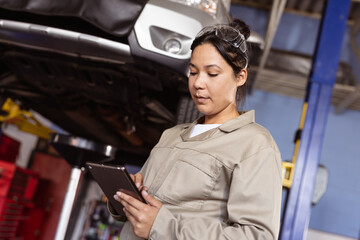 Mid adult asian female engineer using digital tablet while repairing car in workshop, copy space