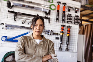 Portrait of confident asian mid adult female mechanic against various work tools in workshop