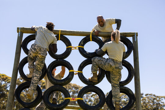 Multiracial young men and woman climbing wall of tires against clear sky in summer at bootcamp