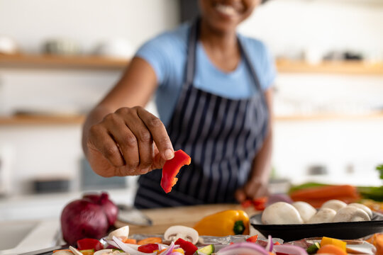 Midsection of biracial woman holding red bell pepper slice while making food in kitchen at home