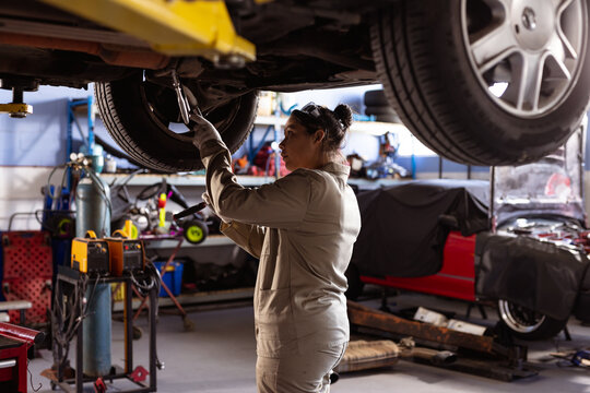 Side view of mid adult asian female technician using work tool while repairing car in workshop