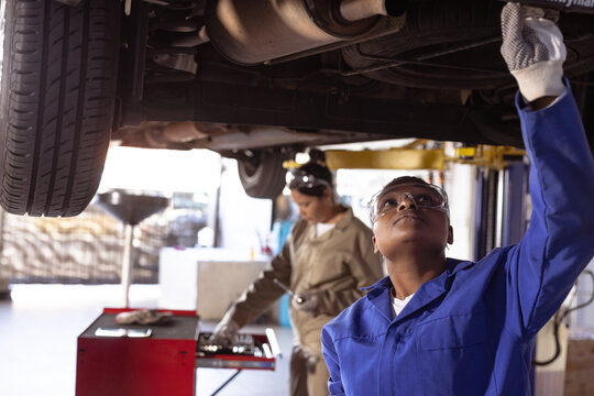 Multiracial mid adult female welders using work tools while repairing car on car lift in workshop