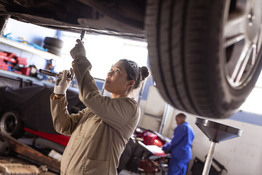 Asian mid adult female mechanic using wrench while repairing car in workshop