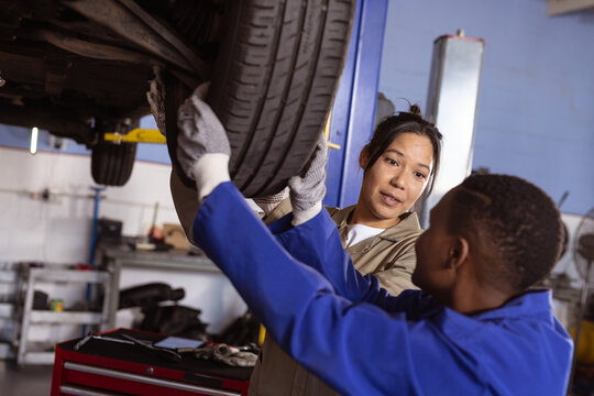 Multiracial mid adult female technicians examining car's tire while repairing it in workshop