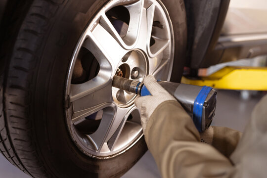 Cropped image of female asian mid adult mechanic using work tool while fixing car's tire