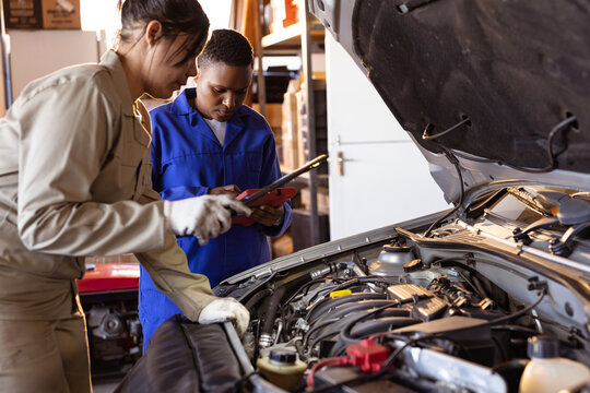 Mid adult multiracial female mechanics using digital tablet while repairing car's engine