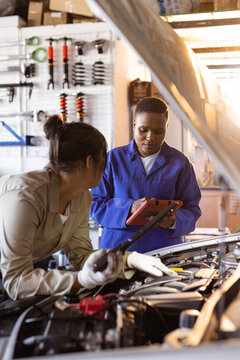 African american mid adult female welder with digital tablet assisting asian colleague in repairing
