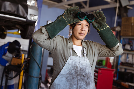 Confident mid adult asian female welder wearing protective worker while working in workshop