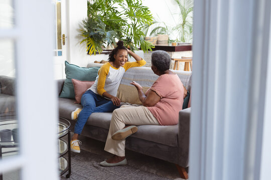 African American Senior Woman Talking With Young Daughter While Relaxing On Sofa Seen Through Door