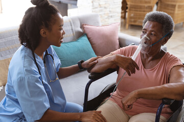 African american doctor talking with senior patient wearing oxygen mask and sitting on wheelchair