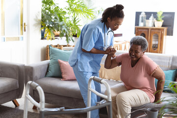 African american young doctor assisting senior female patient in getting up from sofa at home