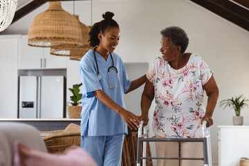African american young doctor assisting smiling senior patient in walking with walker at home