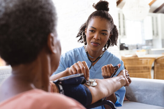 African american doctor examining senior patient's blood pressure with gauge and stethoscope at home