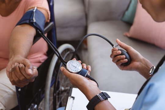 Midsection of african american doctor examining senior woman's blood pressure sitting on wheelchair