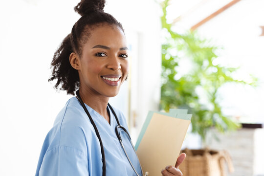 Portrait of smiling african american female doctor with medical report standing against wall at home