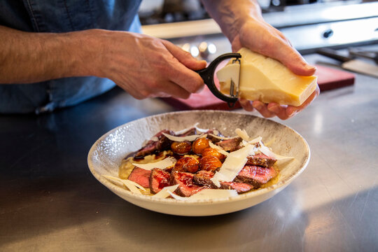 Chef Garnishing Dish Of Steak With Cheese At Counter