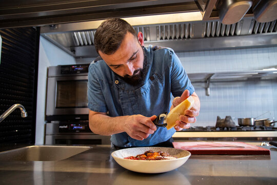 Chef Garnishing Dish Of Steak With Cheese At Counter